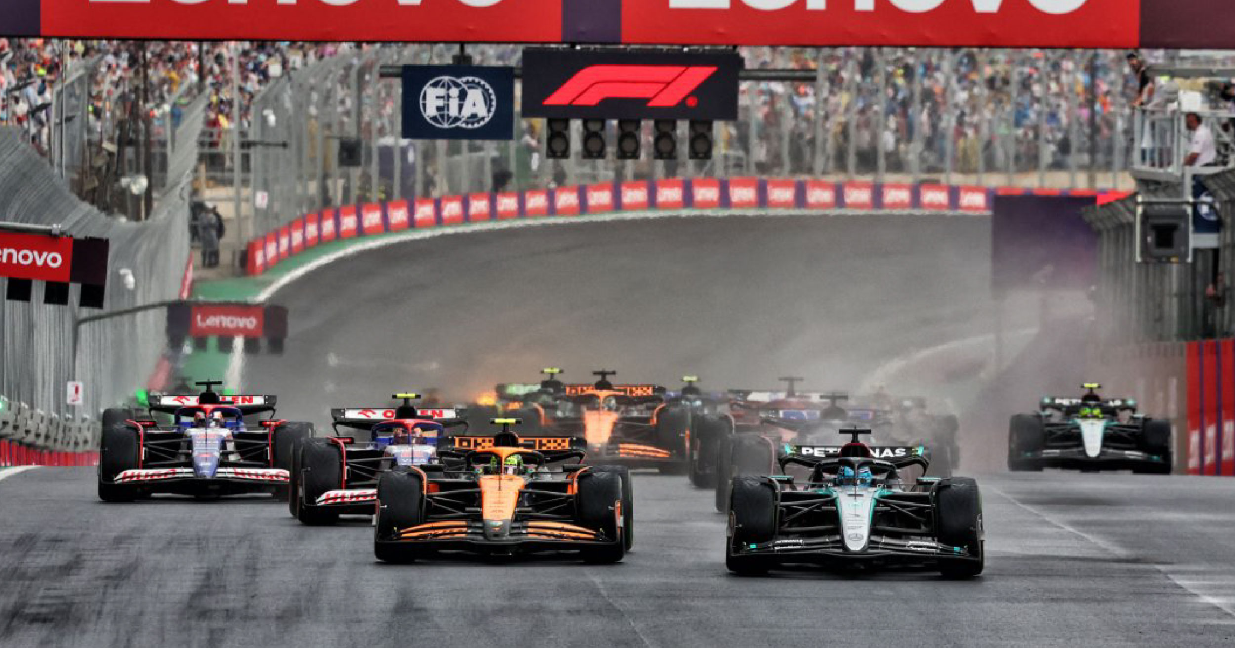 Formula 1 cars accelerating from the starting line at the Brazilian Grand Prix, with McLaren and Mercedes leading the pack under the FIA and F1 banners.