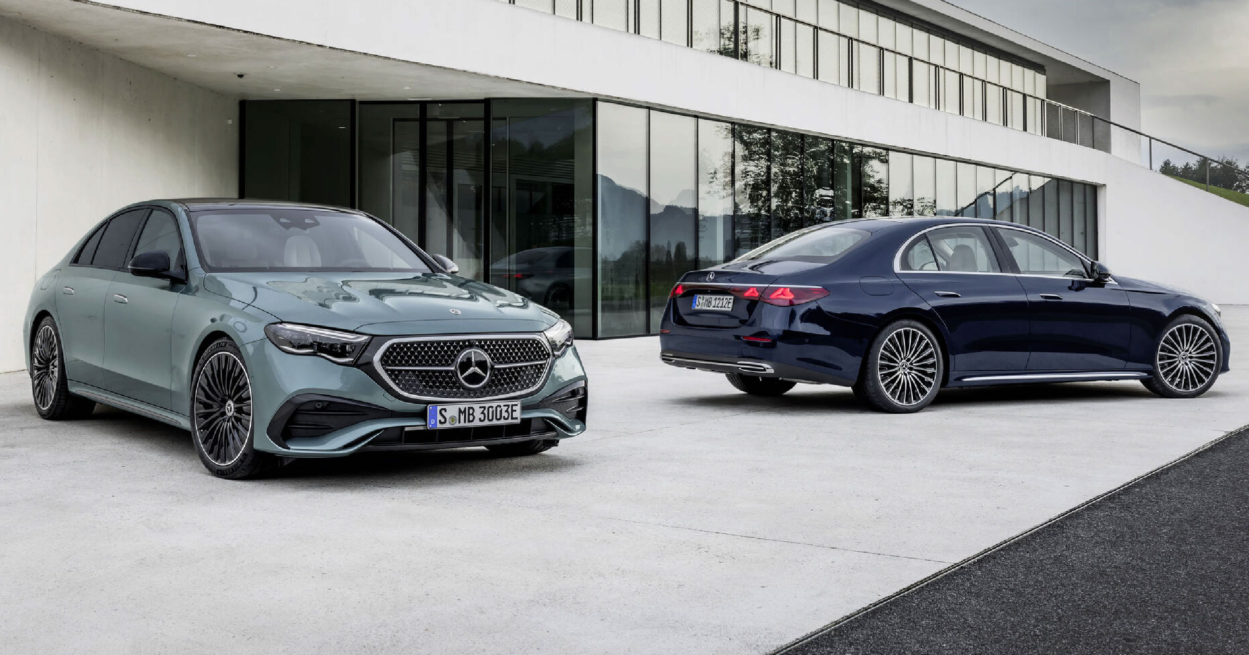 Front and rear view of two Mercedes-Benz E-Class sedans parked in front of a modern building, showcasing sleek design and luxurious styling.