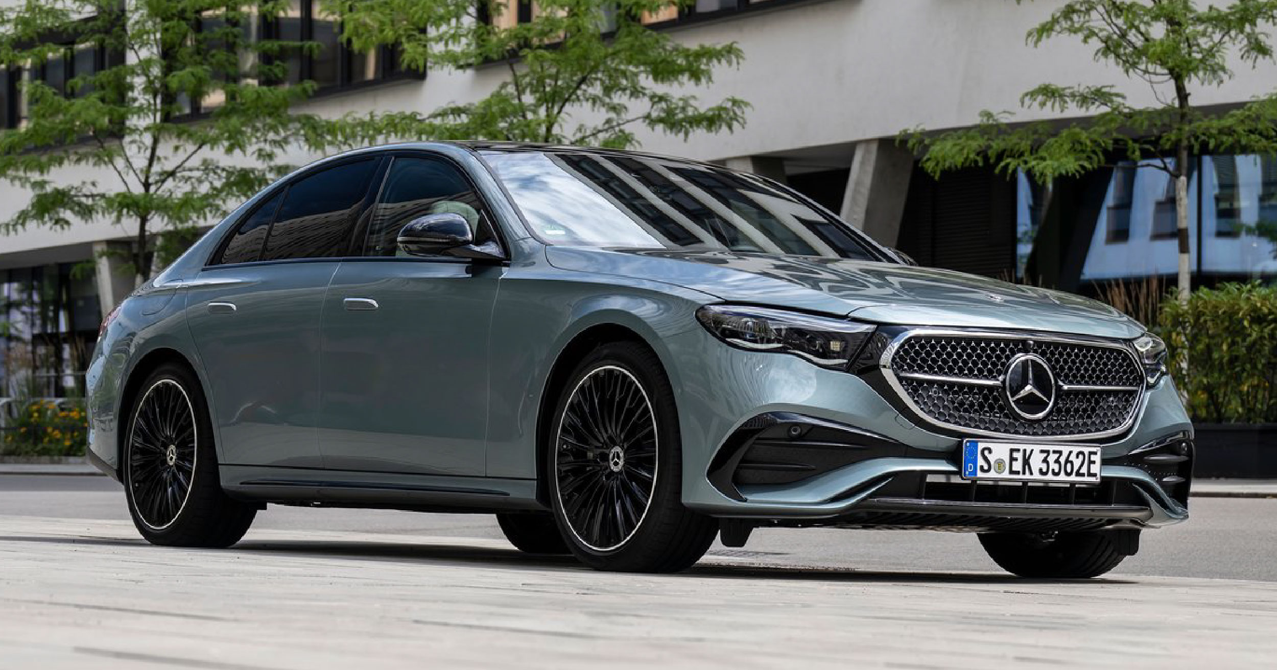 A sleek and elegant 2024 Mercedes-Benz E-Class sedan parked on a city street, showcasing its modern design, refined grille, and aerodynamic body lines.