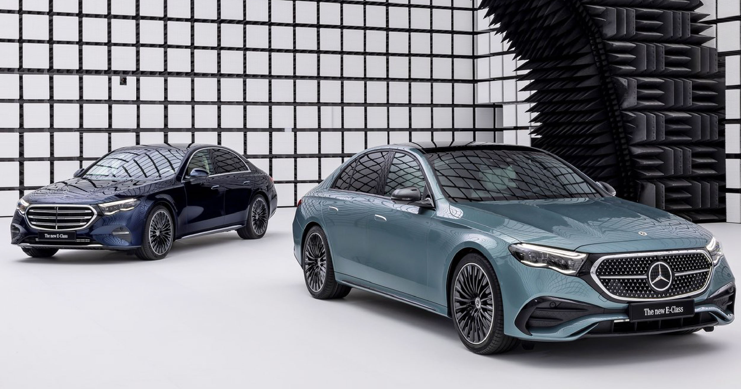 Two 2024 Mercedes-Benz E-Class sedans displayed in a modern showroom, showcasing their sleek designs and distinctive front grilles, with one in a metallic blue finish and the other in a teal shade.